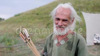 一个穿着民族服装的老人站在田野里放箭